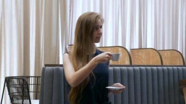 Düşüncelere dalmış genç bir kadın Kupa 'dan kahve içiyor, Kafe' deki koltukta oturuyor.