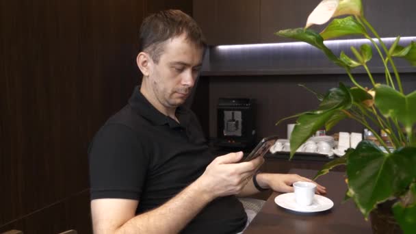 Emocionado hombre sentado en el café con una taza de café y leyendo malas noticias en su teléfono — Vídeos de Stock