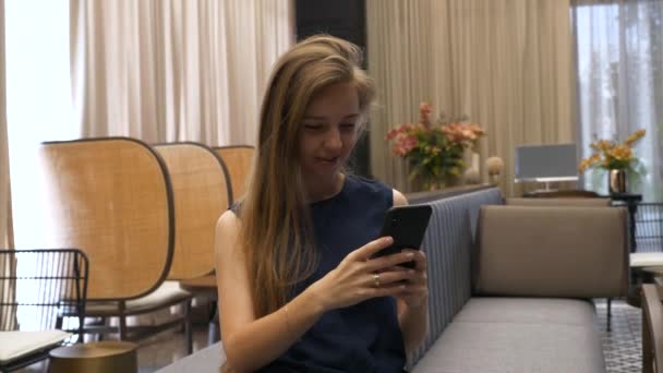 Felice bella ragazza seduta sul divano e utilizzando il telefono cellulare — Video Stock