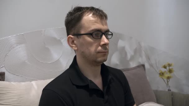 Tired Serious Man in Black Polo T-shirt Sitting on Couch, Takes off His Glasses — Stock Video