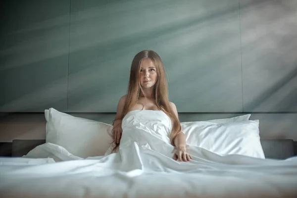 Vrouw met mooi lang haar zitten en ontspannen op het bed met witte deken — Stockfoto