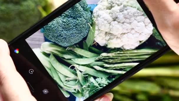 Женщина фотографирует свежие зеленые овощи с мобильного телефона — стоковое видео