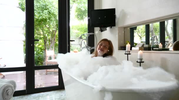 Krásná mladá dívka se baví ve vaně, když mýdlo pěna padá shora — Stock video