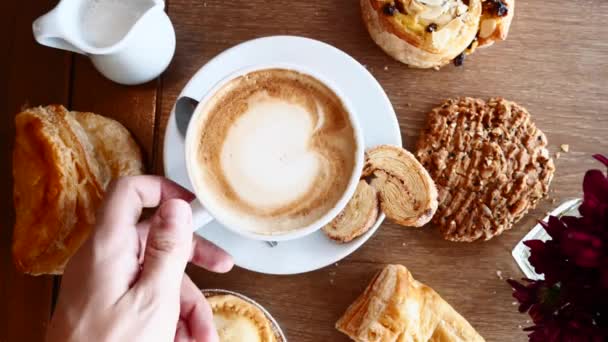 Мужчина взял чашку кофе на завтрак с круассанами на столе в кафе — стоковое видео