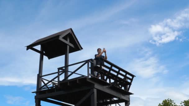 Turista de pie en la torre de madera en el parque con teléfono móvil y video de disparo — Vídeos de Stock