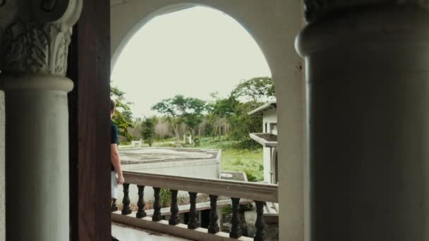Путешественник с рюкзаком на спине, стоящий на балконе заброшенного здания — стоковое видео