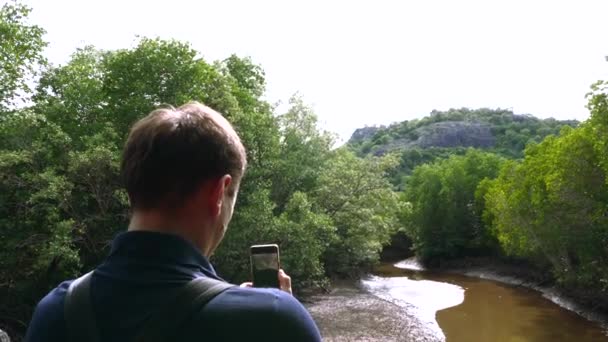 Man Tourist with Backpack Nakręca film na smartfonie Creek w Green Forest — Wideo stockowe