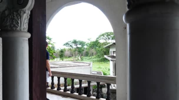 Voyage homme avec un sac à dos sur le dos debout sur le balcon du bâtiment abandonné — Video