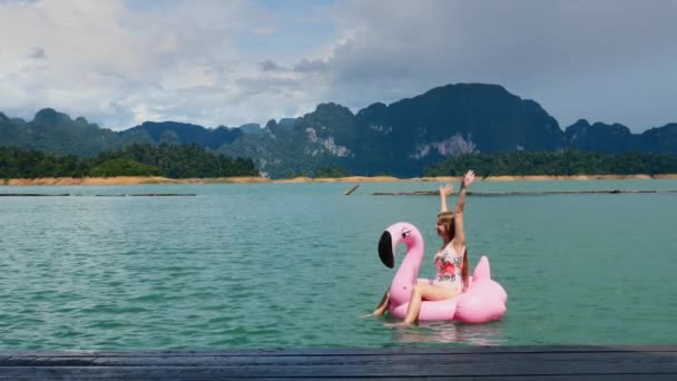 Mulher Divertimento, dança, mãos levantadas no Flamingo inflável rosa no lago azul — Vídeo de Stock