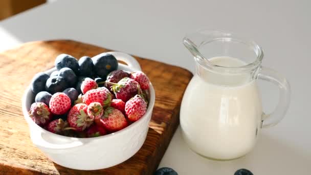 Cuenco con arándanos maduros y fresas, tarro de vidrio con yogur griego en la mesa — Vídeo de stock