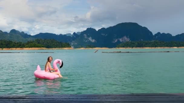 Mujer feliz divertirse y tontear alrededor en el flamenco inflable rosa en el lago azul — Vídeos de Stock
