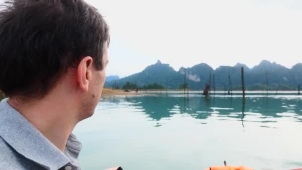Κοντινό πλάνο του χαμογελαστού ανθρώπου που κάθεται στο σκάφος και ιστιοπλοΐα στην πρωινή λίμνη με το βουνό — Αρχείο Βίντεο