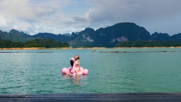 Mulher em férias Relaxando no Flamingo Flutuante Rosa no Lago Azul com Montanha — Vídeo de Stock
