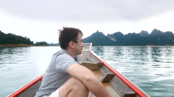 Feliz hombre sonriente sentado en un barco de madera y navegando en el lago azul de la mañana — Vídeos de Stock