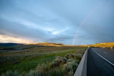 Boş bir kırsal yolun ötesinde parlayan bir gökkuşağı. Merritt BC Kanada