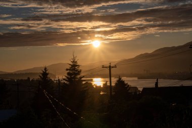 Batan güneş bazı bulutların altından dışarı bakıyor ve siluetler yaratıyor. Vancouver BC Kanada