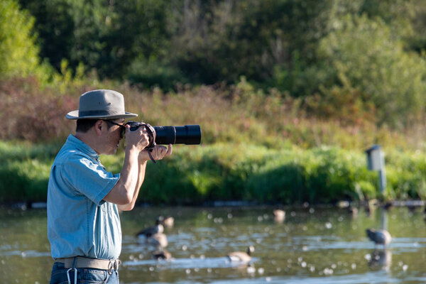 A picture of an Asian man wearing a hat and sunglasses who is taking pictures of a lake.   Vancouver BC Canada