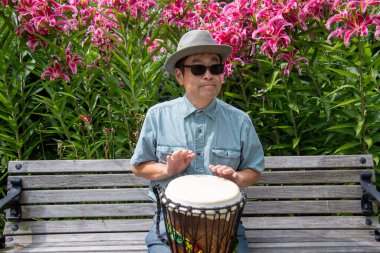 Asyalı bir adam bankta oturmuş djembe çalıyor. Vancouver BC Kanada