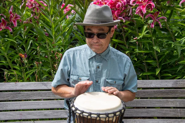 Asyalı bir adam bankta oturmuş djembe çalıyor. Vancouver BC Kanada