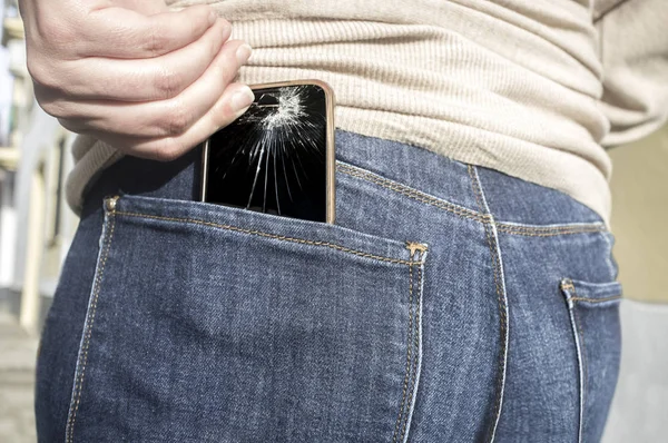 Woman pulls a broken mobile phone up from her pocket jeans pant after sitting over it. Carelessnes about gadgets concept