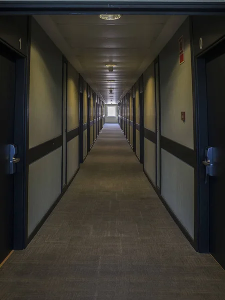 Dark hotel corridor illuminated by natural light. A wide window can be seen in the background