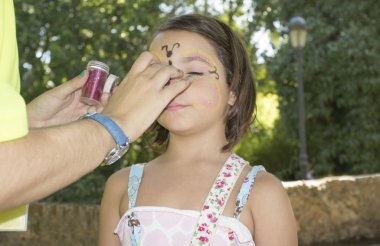 Küçük kız yüz almak açık havada parti sırasında boyalı. Makyaj sanatçısı briyantin kullanır