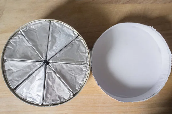 Round cardboard box with melted cheese in aluminium foil and lid on wooden table. Top view