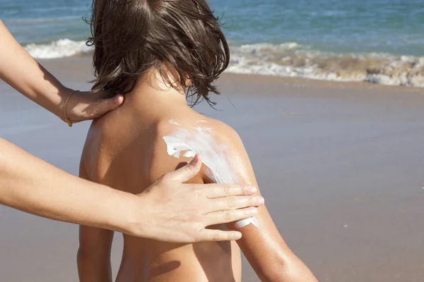 Mother applying sunblock cream to her daughter on arm. Idyllic beach background