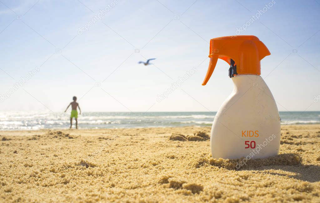 Sunblock cream with Sun Protection Factor or SPF 50 on beach sand. Child boy on background