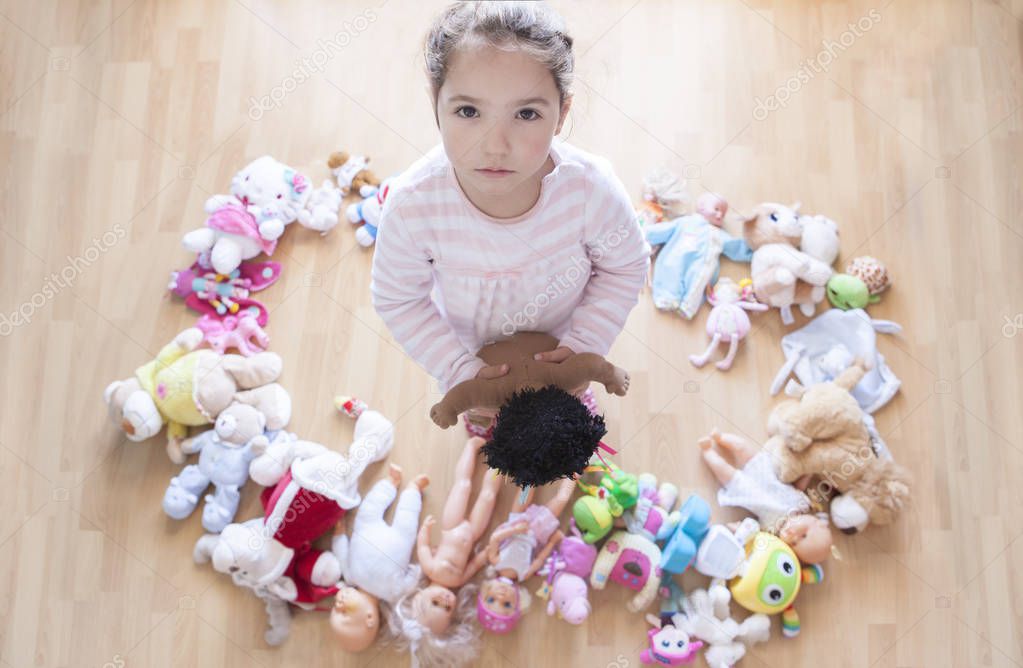 5 years little girl unhappy with lots of toys. Too many toys concept at Infant Behaviour and Development. Overhead view.
