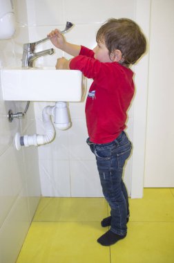 3 years child boy washing hands at adapted school sink but he reaches hardly to the faucet. Troubles on adapted washroom for children clipart