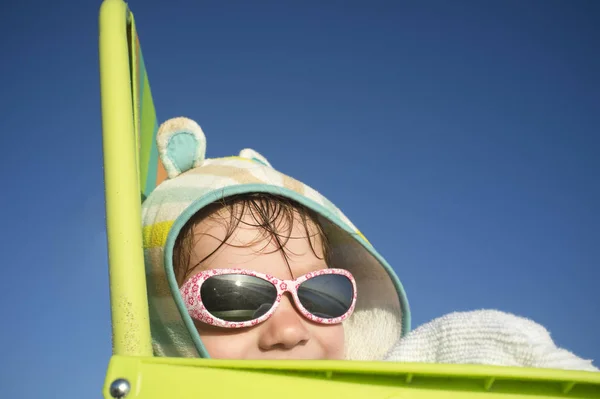微笑3岁男婴坐在沙滩椅上 他戴着带头套的马甲毛巾和太阳镜 — 图库照片