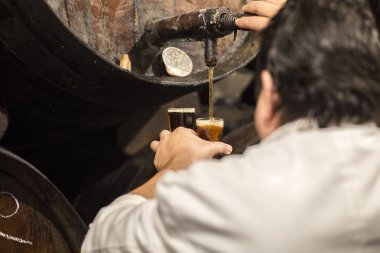 Malaga, İspanya - 2 Mart 2019: Garson puoring tatlı Malaga şarap varil. Eski geleneksel şarap lokali. 