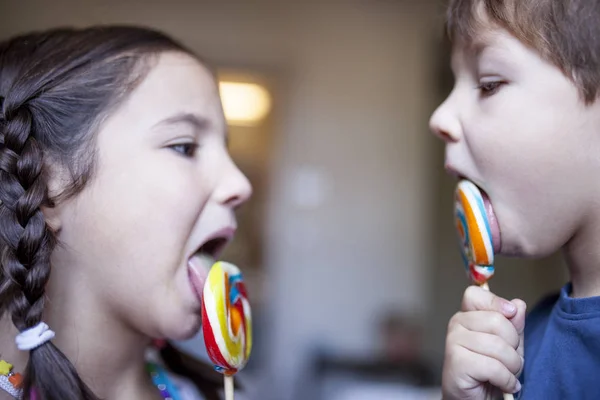 Dos niños lamiendo una gran piruleta colorida — Foto de Stock