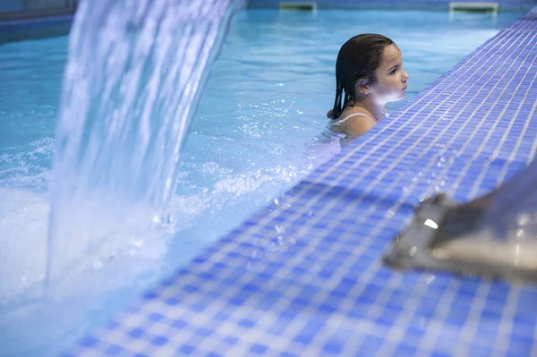 7 lat dziewczynka korzystających wodospad dysze na krytym basenie spa — Zdjęcie stockowe
