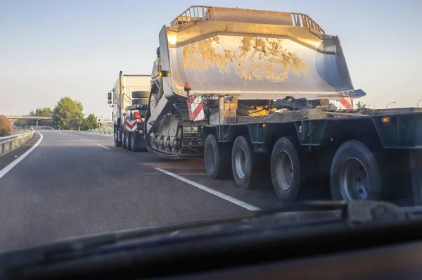 Oversize load truck transporting a huge excavator machine. View from the inside of the car