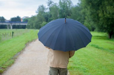 A retired man, protected by an umbrella, walks through a green meadow. Concept of financial protection through retirement pensions.