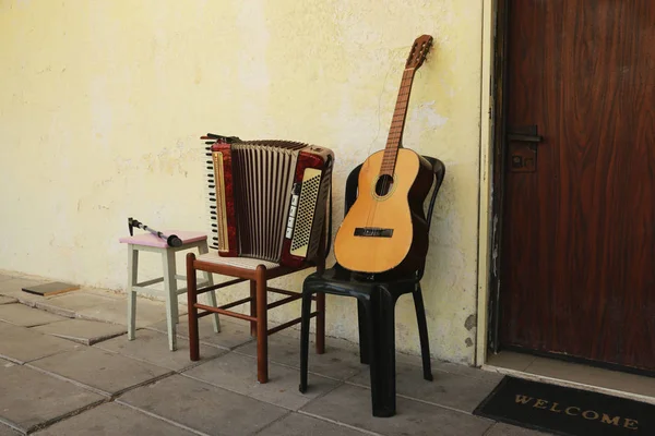 Old guitar and accordion on chairs against a wall background with crumbling paint and a door