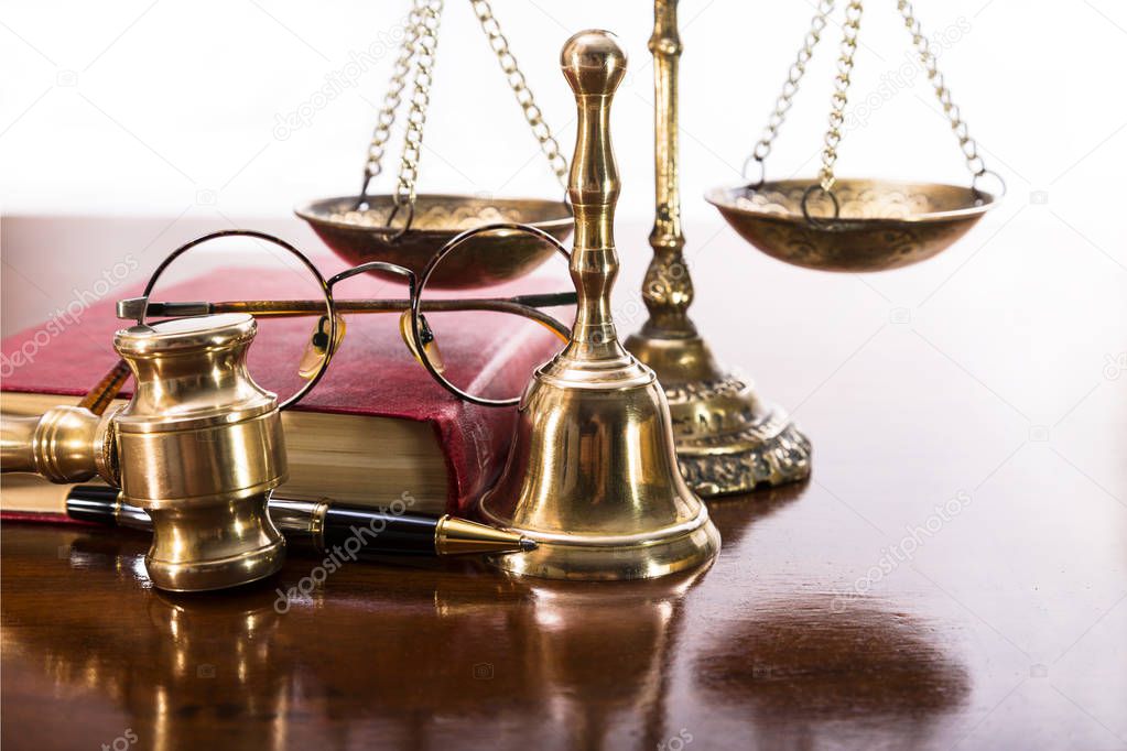 Justice gavel, scales, bell, round-rimmed glasses, a book and pen on the table