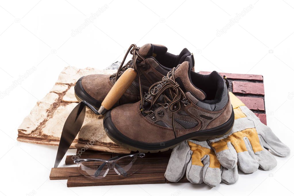 Work boots, goggles and gloves, trowel with tiles on a white background