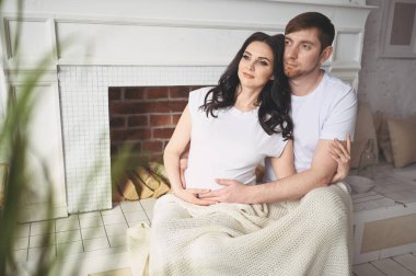 Hamilelik ve insan konsepti. Mutlu bir adam, güzel hamile karısına evde sarılıyor. Doğmamış bebek bekleyen müstakbel ebeveynler. Aşk, ilişki, doğum, mutlu aile kavramı - genç, sevimli evli çift