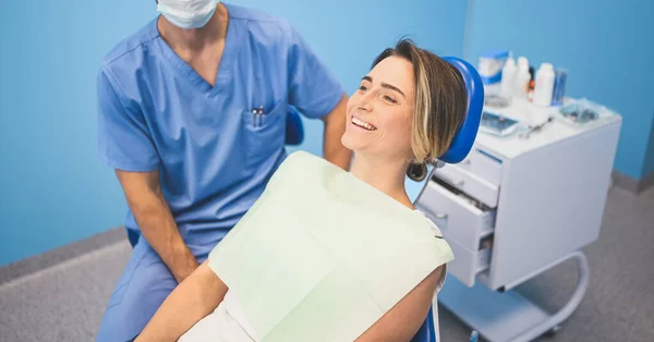 歯科室で歯科機器を用いて患者の歯を調べる歯科医 血液学と健康管理の概念 若いですハンサムな男性医師で使い捨て医療顔マスク 笑顔幸せな女性 — ストック写真