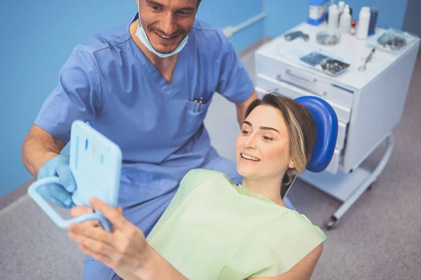 Dentysta Pokazuje Pacjentowi Wyniki Leczenia Lustrem Badając Zęby Sprzętem Stomatologicznym — Zdjęcie stockowe
