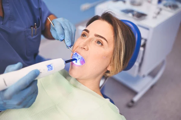牙科医生在牙科诊所检查病人的牙齿后 使用牙科固化轻型设备进行充填 口腔医学和保健概念 把年轻快乐的女人关在牙椅上 — 图库照片