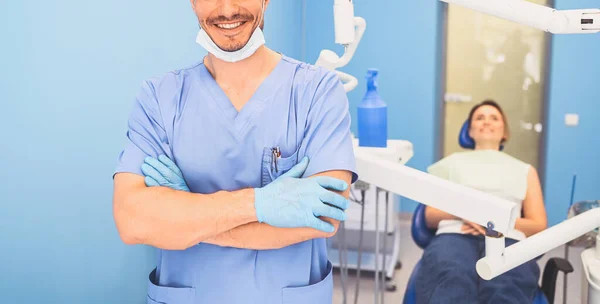 年轻英俊的男医生 身穿蓝色的医疗制服 带着装备的一次性医疗面罩在牙科诊所里 快乐的病人坐在牙椅上 口腔医学的概念 复制空间 — 图库照片