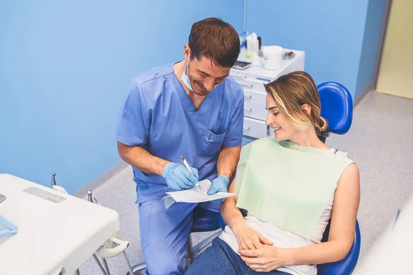 牙科医生在牙科诊所写了一个结论和诊断 口腔医学和保健概念 年轻英俊的男医生 戴着一次性医疗面罩 戴着手套 面带微笑 快乐的女人 — 图库照片