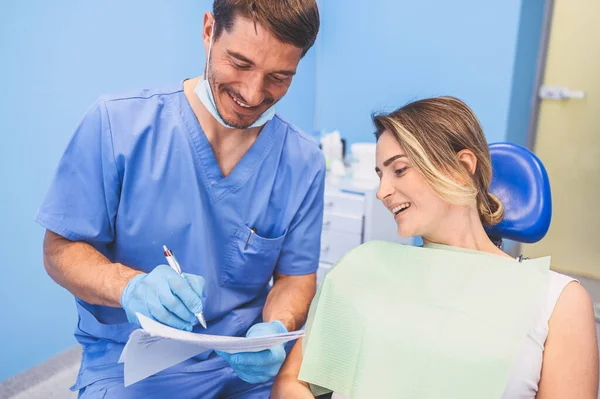 牙科医生在牙科诊所写了一个结论和诊断 口腔医学和保健概念 年轻英俊的男医生 戴着一次性医疗面罩 戴着手套 面带微笑 快乐的女人 — 图库照片