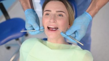 Diş hekimi muayenehanesinde bir hastanın dişlerini diş malzemesi kaşığıyla muayene ediyor. Stomatoloji ve sağlık hizmetleri kavramı. Tek kullanımlık tıbbi maskeli doktor, gülümseyen mutlu kadın..