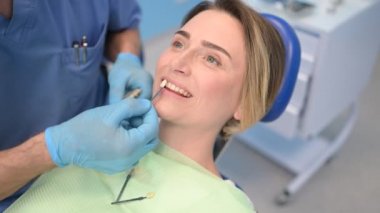 Diş hekimi hastanın diş beyazlatma seviyesini dişçinin rengiyle kontrol ediyor. Diş hekimliğinde dişçi aletleri. Stomatoloji konsepti. Eldivenli doktor elleri ve gülümseyen mutlu kadın..