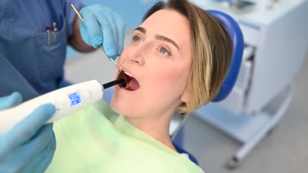 牙科医生在牙科诊所检查病人的牙齿后 使用牙科固化轻型设备进行充填 口腔医学和保健概念 把年轻快乐的女人关在牙椅上 — 图库视频影像